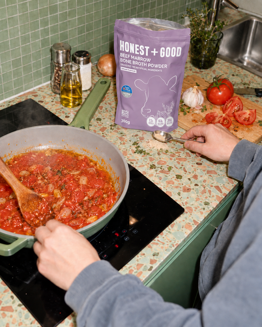 Adding Honest + Good Beef Marrow Bone Broth Powder to a tomato sauce on the hob