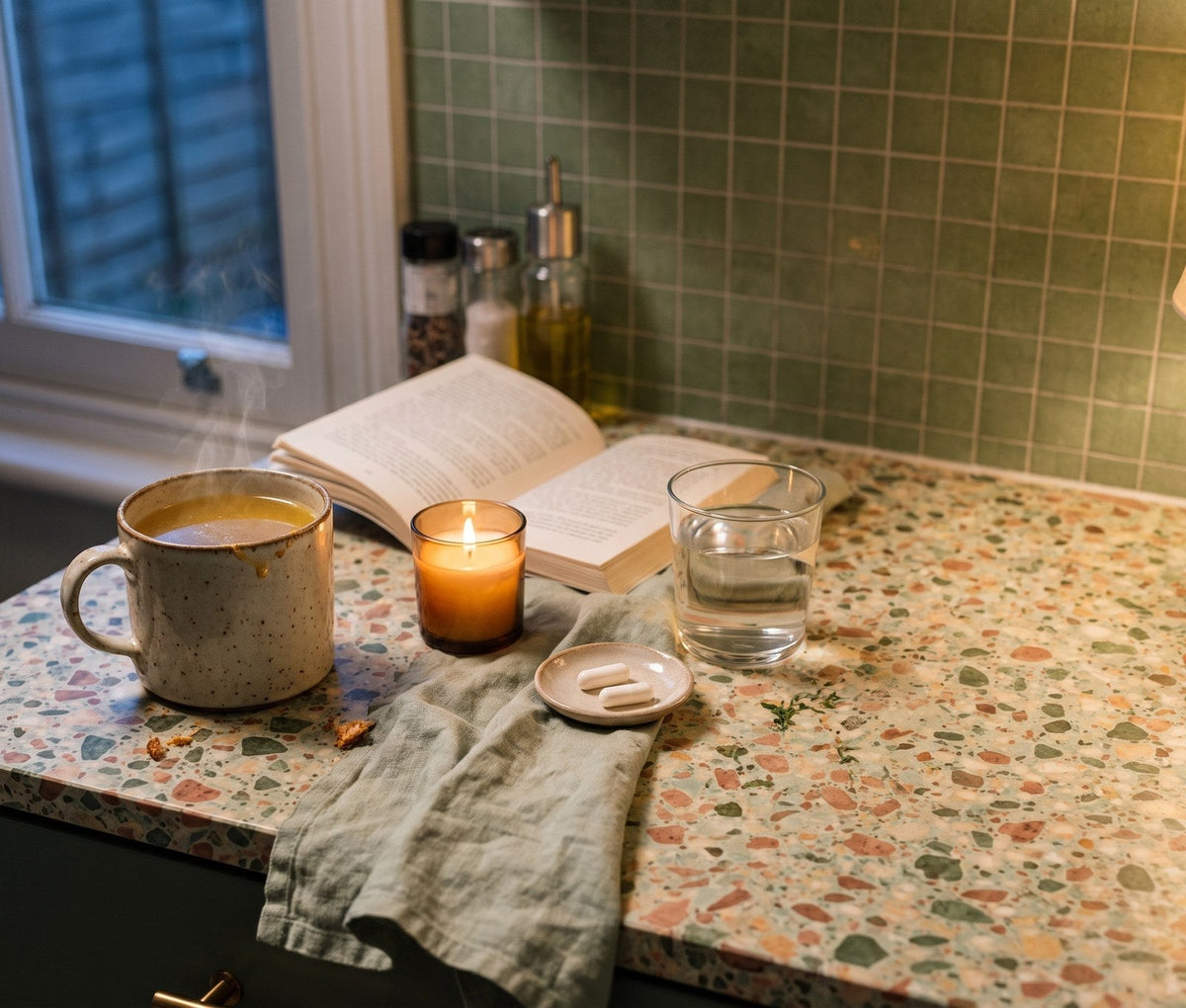 An evening mug of broth with a candle, an open book, a glass of water and two capsules
